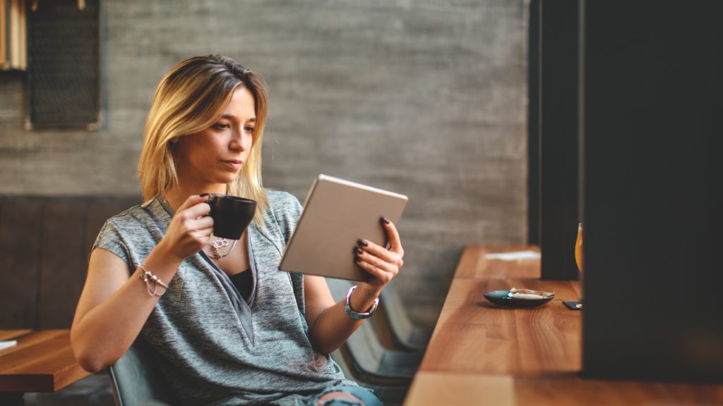 woman drinking coffee and reading on tablet